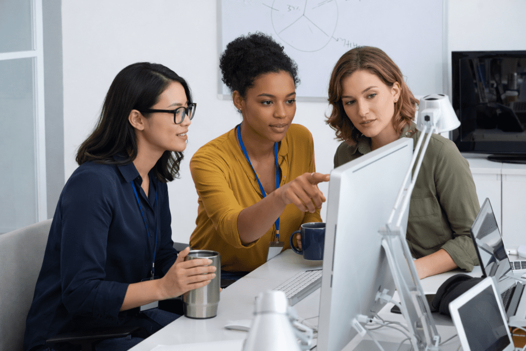 Equipo de mujeres profesionales colaborando en oficina moderna utilizando tecnología en un entorno de trabajo híbrido humano + IA.